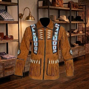 May include: A brown suede jacket featuring long fringe detailing on the chest and sleeves, a front zipper closure, and decorative panels with light blue, white, and black geometric patterns and eagle motifs, accented by white bone-like embellishments.