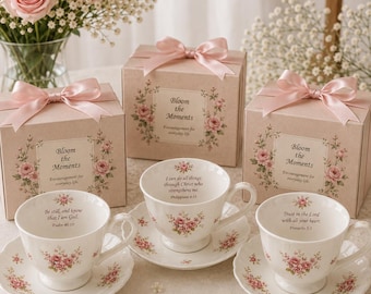 May include: Three white porcelain teacups and saucers decorated with pink rose patterns and religious text, paired with three matching square gift boxes tied with pink satin ribbons. Each cup features a unique scripture verse printed inside.