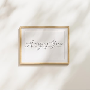 Può includere: Una stampa artistica da parete rettangolare in una cornice di legno chiaro con il testo Amazing Grace HOW SWEET THE SOUND in una combinazione di elegante scrittura corsiva e tipografia sans-serif centrata su uno sfondo bianco.