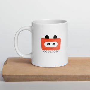 Könnte beinhalten: Ein weißer Keramikbecher mit einer Grafik eines roten Roboterkopfes mit zwei schwarzen Antennen und dem darunter in Schwarz gedruckten Text CODEROBO. Das Roboterdesign zeigt einen weißen Bildschirmbereich mit zwei schwarzen Augen und einem kleinen Mund.