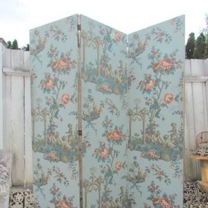May include: A three-panel folding screen featuring a light blue background with a repeating pattern of orange and pink flowers, green foliage, and small figures of cherubs playing near stone arches and garden structures throughout the panels.