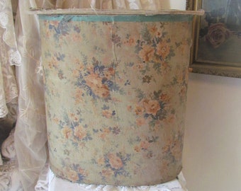 May include: A cylindrical wastebasket featuring a vintage-inspired floral pattern with muted orange, blue, and green flowers on a beige background. The top rim is accented with a solid teal band, and the structure appears to be made of paper or cardboard.