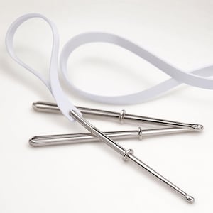 May include: Two silver-toned metal bodkins with rounded tips and a small sliding ring on each shaft. A long, flexible white plastic strap is threaded through the eye of one of the metal bodkins, creating a large loop for threading or pulling.