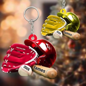 May include: Two baseball-themed keychains featuring a metallic red or yellow batting helmet, a matching baseball glove, and a baseball printed with the year 2026. Each set includes a wooden baseball bat engraved with the name James in black text.