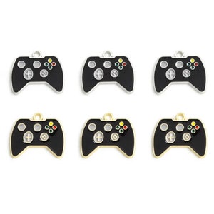 May include: Six black and silver game controller charms with a gold finish. The charms are in the shape of a video game controller with buttons and a directional pad. The charms are perfect for adding a touch of fun to your jewelry or crafts.