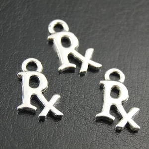 May include: Three silver charm pendants shaped like the letter R with a cross through it. The charms are on a black background.