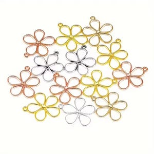 May include: A collection of open-frame flower charms in gold, silver, and rose gold tones. Each charm features five rounded petals and a small circular loop at the top for attachment. The metal pieces are arranged in a scattered, overlapping cluster.
