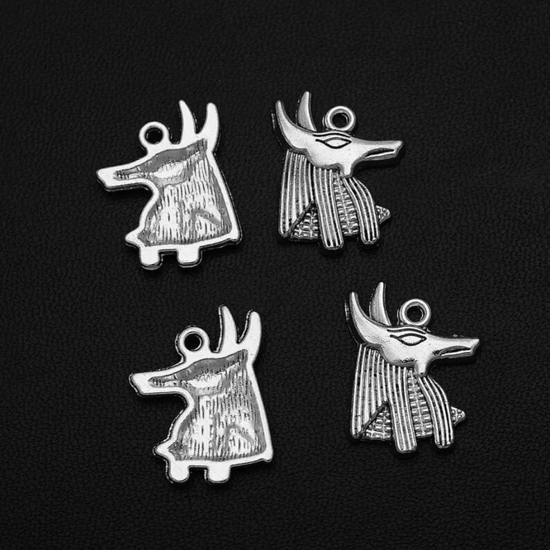 May include: Four silver charm pendants in the shape of anubis, an Egyptian god, with detailed engravings. The charms are perfect for jewelry making or crafting.