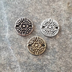 May include: Three round metal charms with a floral design. The charms are in silver, copper, and brass.