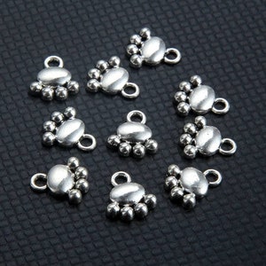 May include: Ten silver-toned metal charms with a rounded oval shape and a cluster of five small balls at the top. The charms have a loop at the bottom for attaching to jewelry or other crafts.