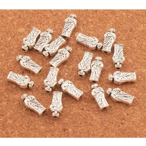 May include: A group of silver-toned metal angel charms with intricate details. The charms are shaped like a standing angel with wings and a halo. The charms are scattered on a brown surface.