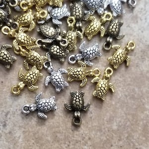 May include: A collection of silver and gold turtle charms. The charms are detailed with textured shells and have a loop for attaching to jewelry or other crafts.