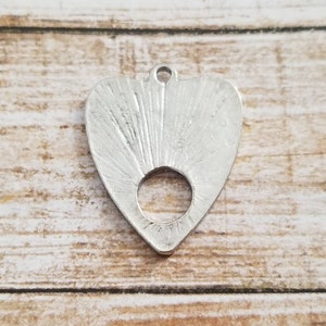 May include: Silver heart-shaped pendant with a circular hole in the center. The pendant has a textured surface with radiating lines.