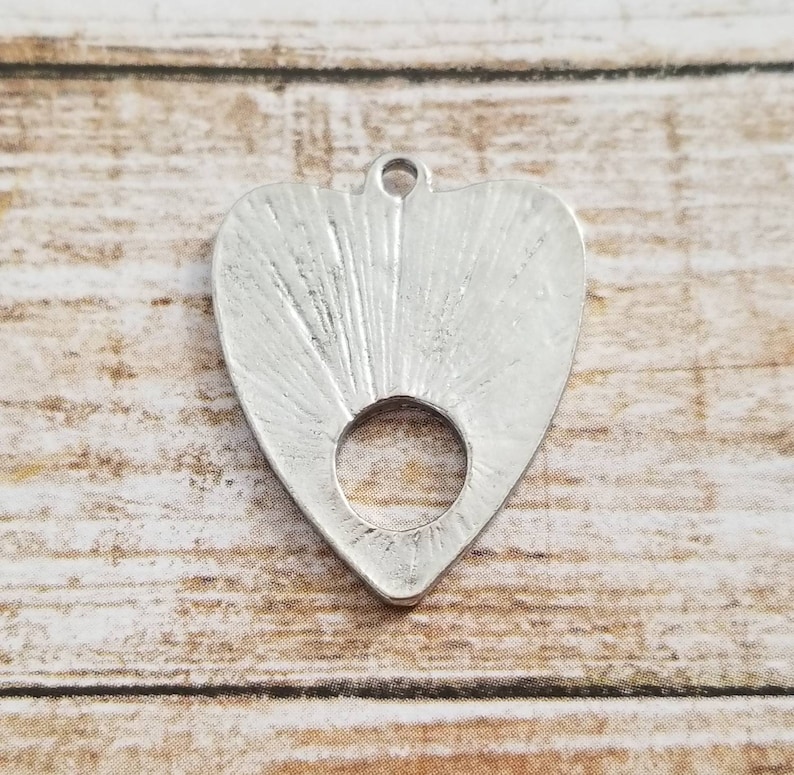 May include: Silver heart-shaped pendant with a circular hole in the center. The pendant has a textured surface with radiating lines.