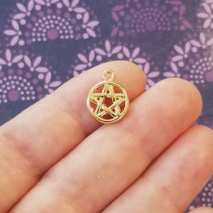 May include: Gold-toned metal charm featuring a pentagram design. The charm is round and has a loop at the top for attaching to a necklace or bracelet.