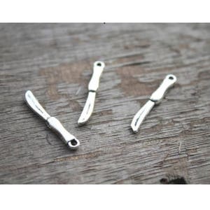 May include: Three silver knife charms, each with a slightly different shape, are arranged on a wooden surface.