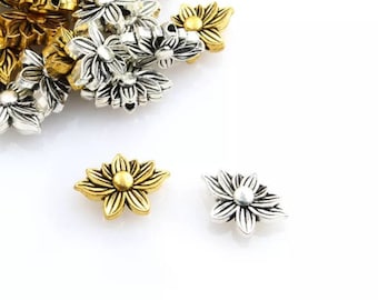 May include: A pile of silver and gold flower-shaped metal beads. Two beads are isolated in the foreground, one gold and one silver.