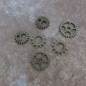 May include: Six antique gold-toned metal gears of varying sizes. The gears have a detailed design and are perfect for crafting projects.