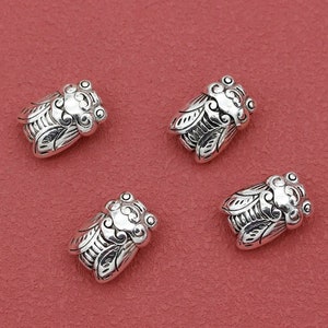 May include: Four silver-toned cicada charms with intricate details. The charms are small and have a detailed design.