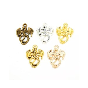 May include: Five dragon charms in different metal finishes: antique brass, silver, gold, and rose gold. Each charm features a detailed dragon design with wings outstretched.