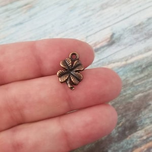 May include: A copper-colored four-leaf clover charm with a loop at the top for attaching to jewelry or crafts.