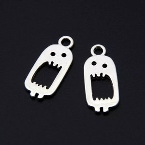May include: Two silver-colored ghost charms with open mouths and small eye details. Each charm has a loop at the top for attaching to jewelry or other crafts. The charms are on a dark background.