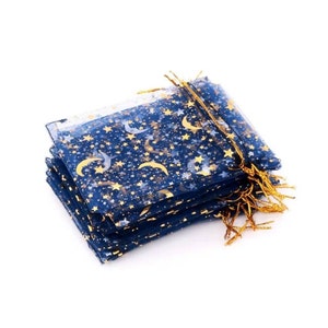 May include: A stack of blue organza gift bags with gold stars and crescent moons printed on them. The bags have gold drawstring closures and gold tassels.