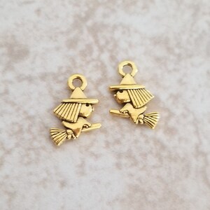 May include: Two gold-toned metal charms shaped like witches riding broomsticks. The charms have a loop at the top for attaching to jewelry or other crafts.