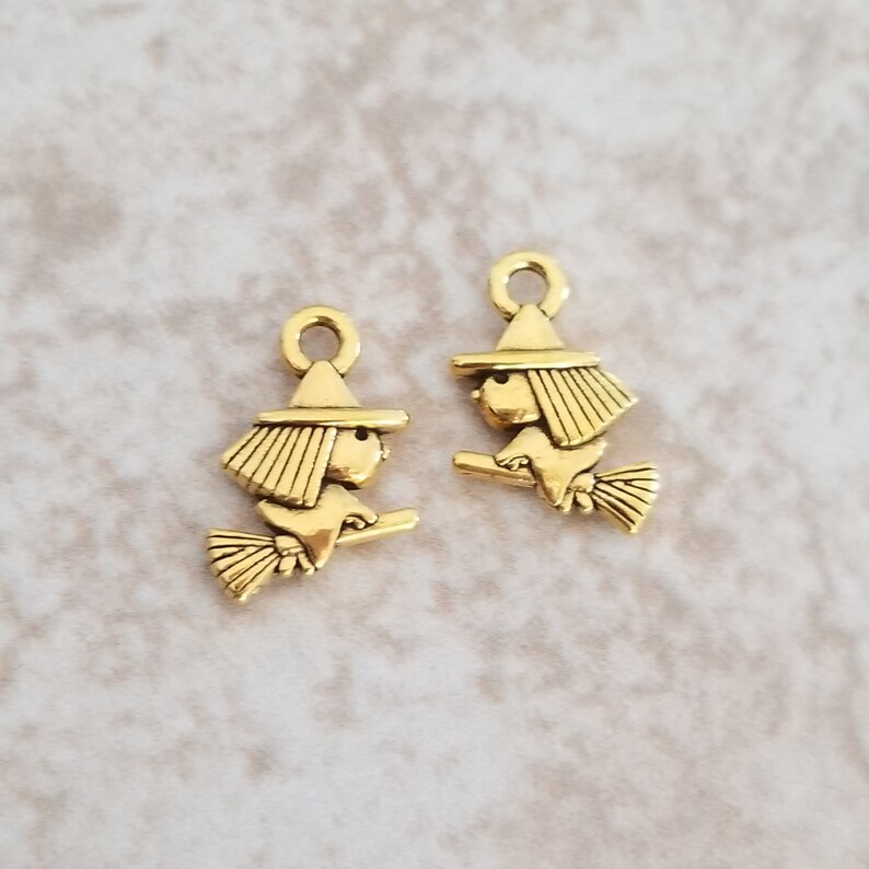 May include: Two gold-toned metal charms shaped like witches riding broomsticks. The charms have a loop at the top for attaching to jewelry or other crafts.