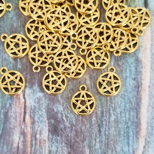 May include: A pile of gold-colored metal charms in the shape of a five-pointed star. The charms have a hole at the top for attaching to jewelry or other crafts.