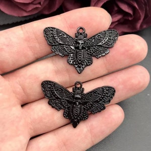 May include: Two black metal moth charms with a skull design. The moths have intricate details and a black finish.