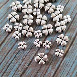 May include: A large quantity of silver four-leaf clover charms. The charms are scattered on a wooden surface.