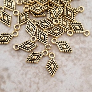 May include: A pile of gold-colored metal diamond-shaped charms with a small loop at the top. The charms have a textured surface and a geometric design.