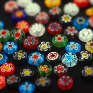 May include: Assortment of colorful glass flower-shaped beads with intricate designs. The beads are scattered on a black surface.