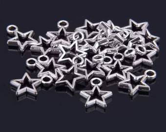 May include: A collection of silver-toned metal star charms, each featuring a hollow center and a small circular loop at the top for attachment. The charms have a metallic finish and are arranged in a scattered pile, showing multiple star shapes.