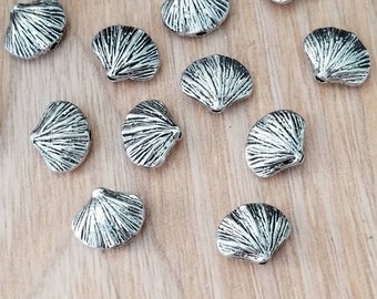 May include: A collection of silver-toned metal seashell charms. The charms are in the shape of a scallop shell and a cone shell.