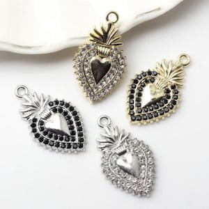 May include: Four heart-shaped pendants with a gold or silver finish. Each pendant features a heart-shaped center and is adorned with either clear or black crystals. The pendants have a loop at the top for attaching to jewelry.