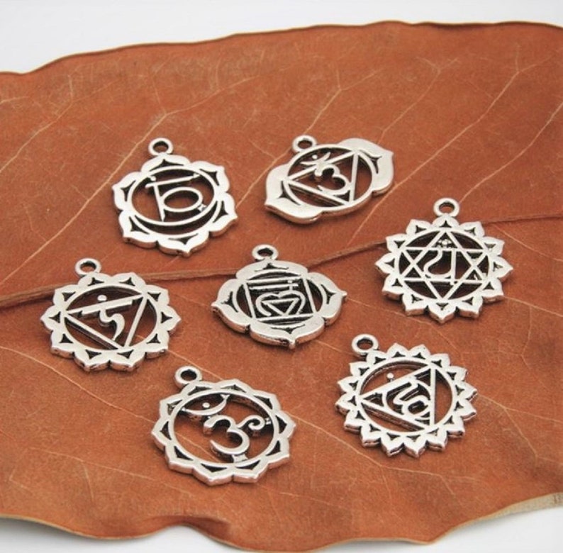 May include: Seven silver-toned metal charms with intricate designs representing the seven chakras. Each charm features a unique symbol and is surrounded by a decorative border.