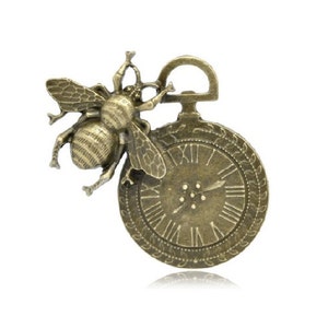 May include: A bronze-colored pocket watch with a bee design on the top. The watch face has Roman numerals and a single hand.