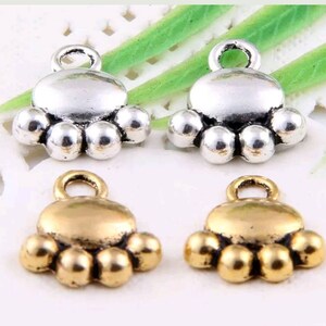 May include: Four silver and gold paw print charms with a loop for attaching to jewelry or other crafts. The charms are in the shape of a paw print with five toes.