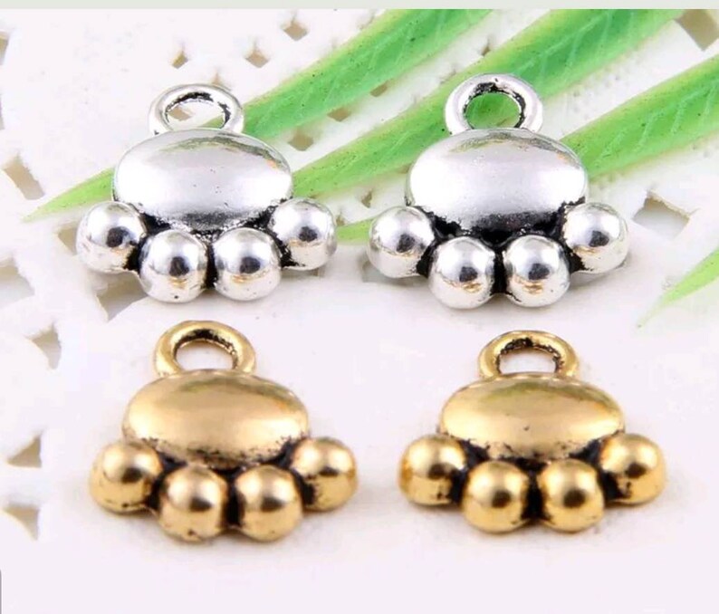 May include: Four silver and gold paw print charms with a loop for attaching to jewelry or other crafts. The charms are in the shape of a paw print with five toes.