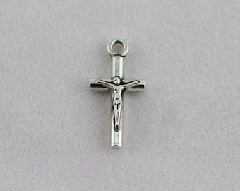 May include: A small, silver-colored crucifix pendant. The cross features a detailed depiction of Jesus Christ. The pendant has a loop at the top for attaching to a chain or cord. The crucifix is a religious symbol.