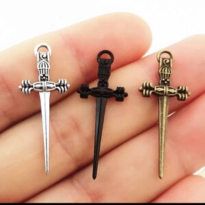 May include: Three silver, black, and bronze sword charms with intricate details. The swords have a pointed tip and a decorative handle.