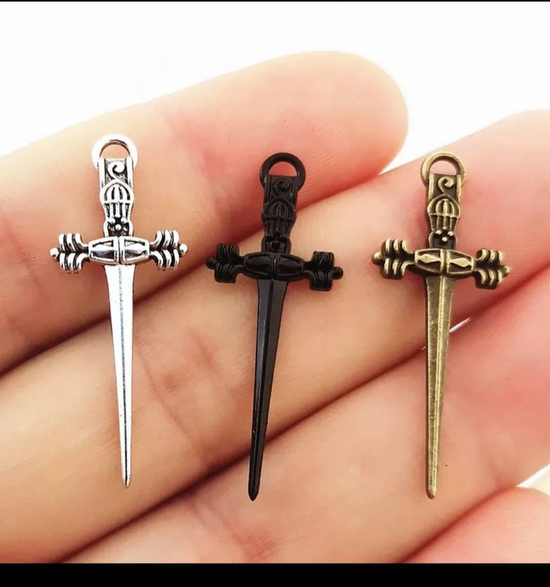 May include: Three silver, black, and bronze sword charms with intricate details. The swords have a pointed tip and a decorative handle.
