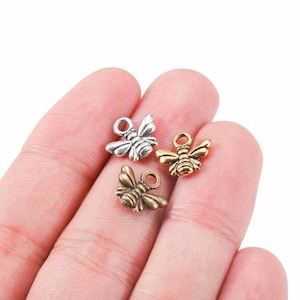 May include: Three bee charms in silver, gold, and bronze. The charms are small and detailed, with a loop at the top for attaching to jewelry or other crafts.