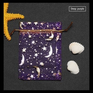 May include: A small purple drawstring bag with a gold metallic moon and star pattern. The bag is made of sheer fabric and has a gold drawstring.