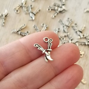 May include: Silver-toned metal charm in the shape of a pair of scissors. The charm is small and detailed, with a loop at the top for attaching to a necklace or bracelet.