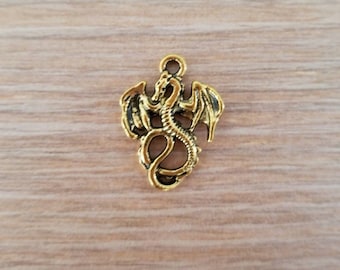 May include: A small, antique gold-toned metal charm shaped like a coiled dragon with outstretched wings. The dragon features a textured, scaled body and a small circular loop at the top for attachment, showcasing a weathered, dark finish.