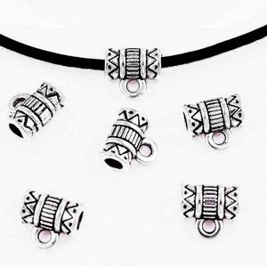 May include: Silver-toned metal jewelry findings with an etched design. The findings are cylindrical with a loop on one end and are shown on a black cord. The design includes geometric patterns and lines.
