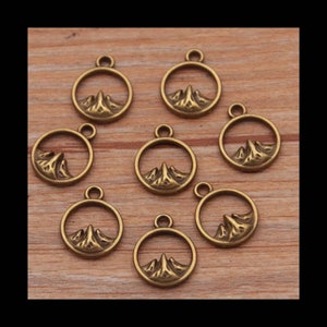 May include: Eight antique gold-toned metal charms featuring a mountain range design inside a circle. Each charm has a loop at the top for attaching to jewelry or other crafts.